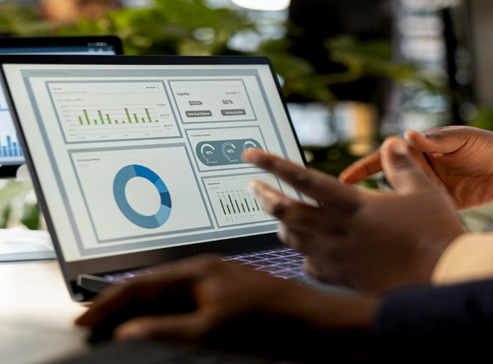 A person working at a laptop showing a dashboard of charts and donut graphs.
