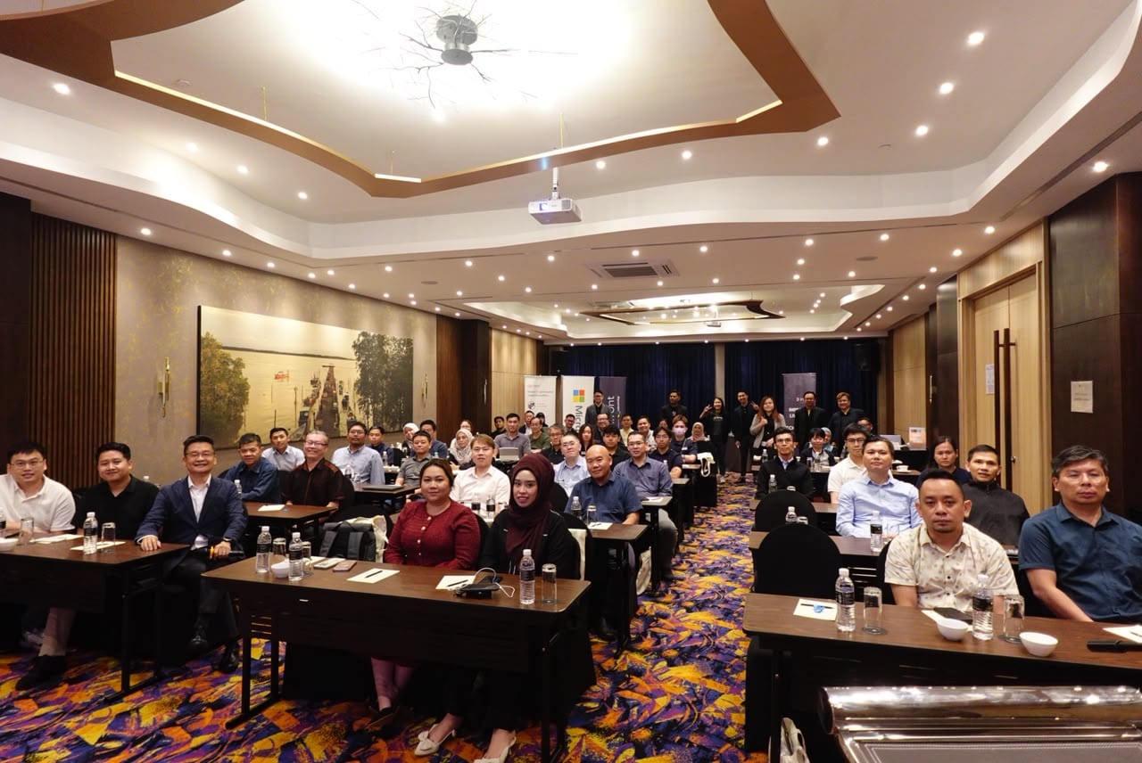 A full hotel function room of attendees seated at long tables, facing the camera.