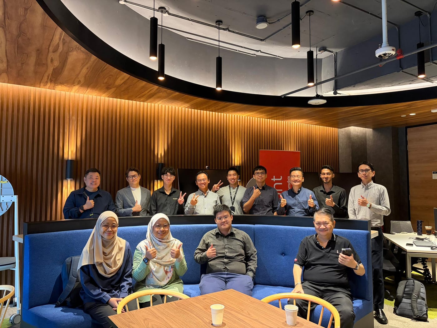 Event attendees gathered around a blue sofa in a wood-panelled room, giving a thumbs-up to the camera.